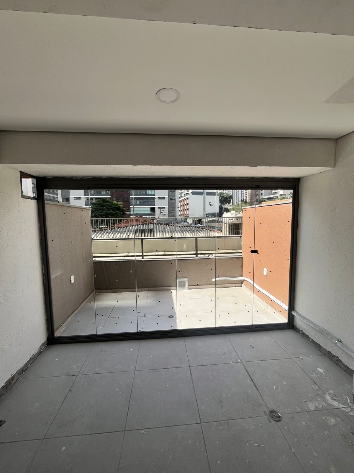 Ambiente interno com fechamento em folhas de vidro e perfil escuro, voltado para um terraço descoberto