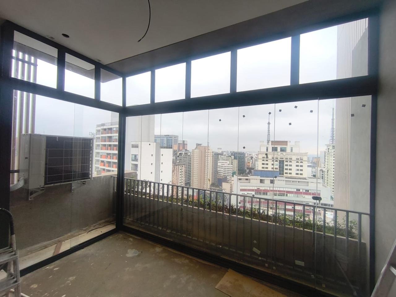 Sacada de canto envidraçada nas duas faces, com faixa superior de vidro fixo em perfis pretos e vista para a cidade