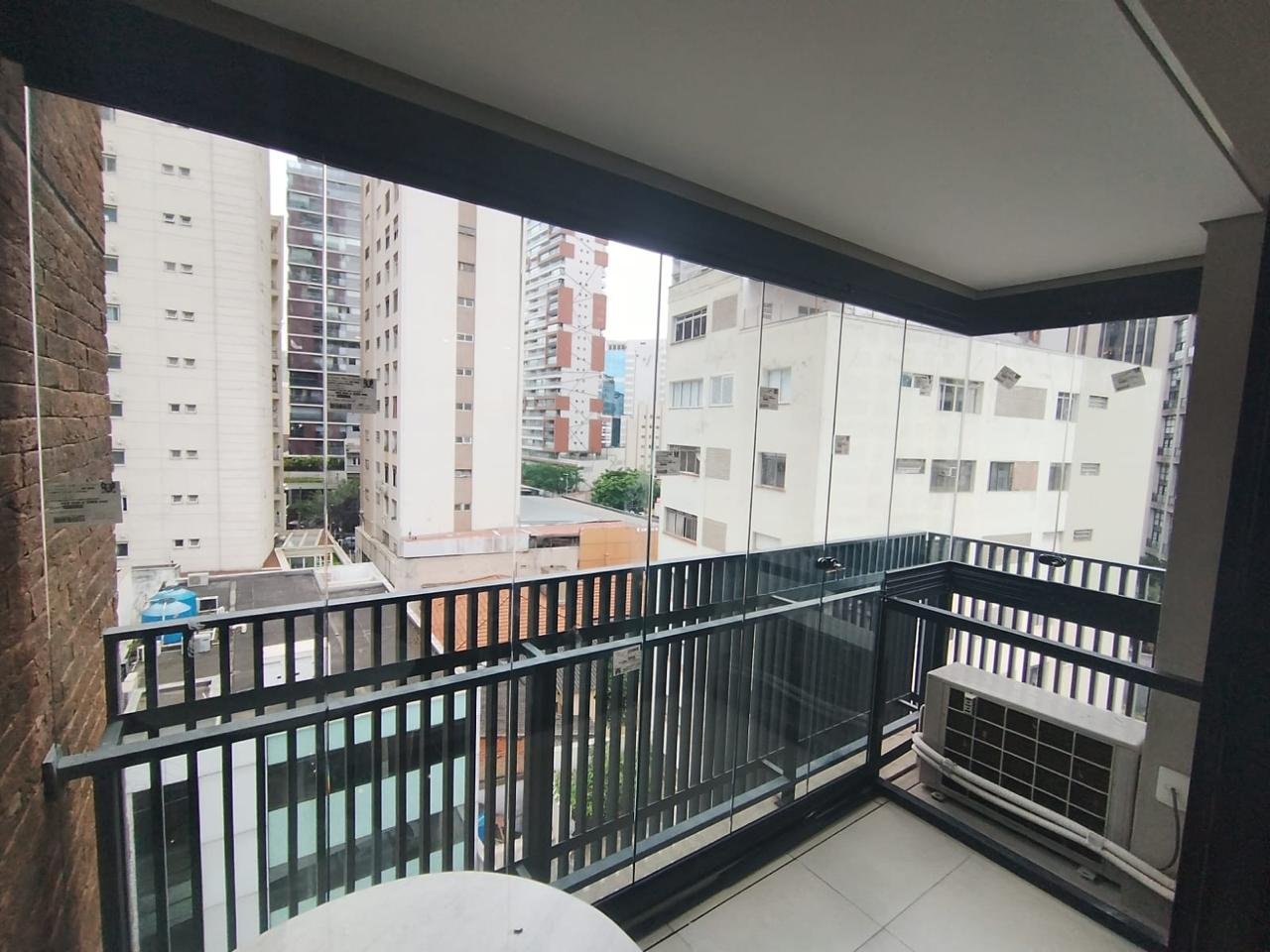 Sacada com guarda-corpo preto de barras verticais e envidraçamento nas duas faces, mesa redonda em primeiro plano