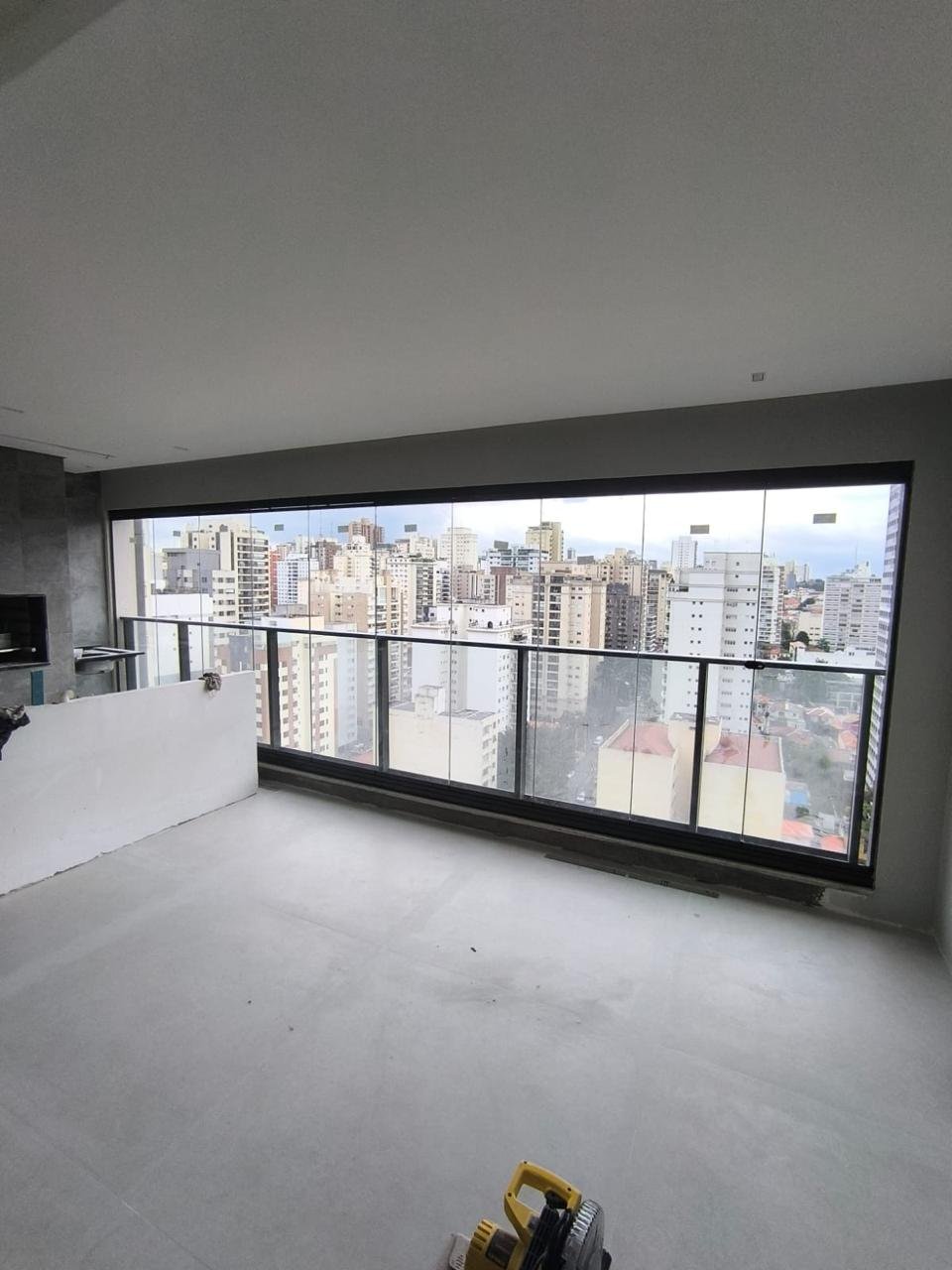 Varanda gourmet integrada à sala, com envidraçamento contínuo em perfis pretos e vista panorâmica de prédios